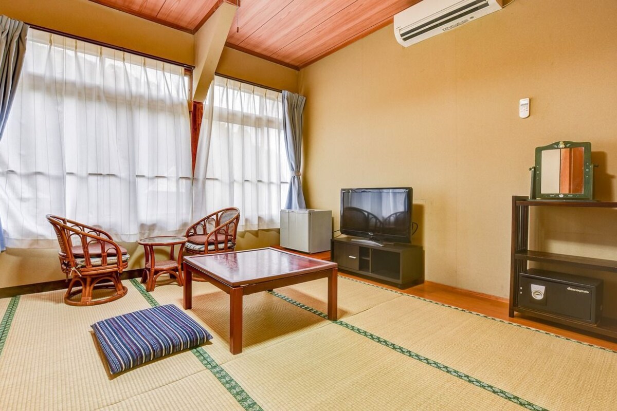 Una habitación con suelo de tatami, una televisión, un armario y una pequeña mesa con sillas.