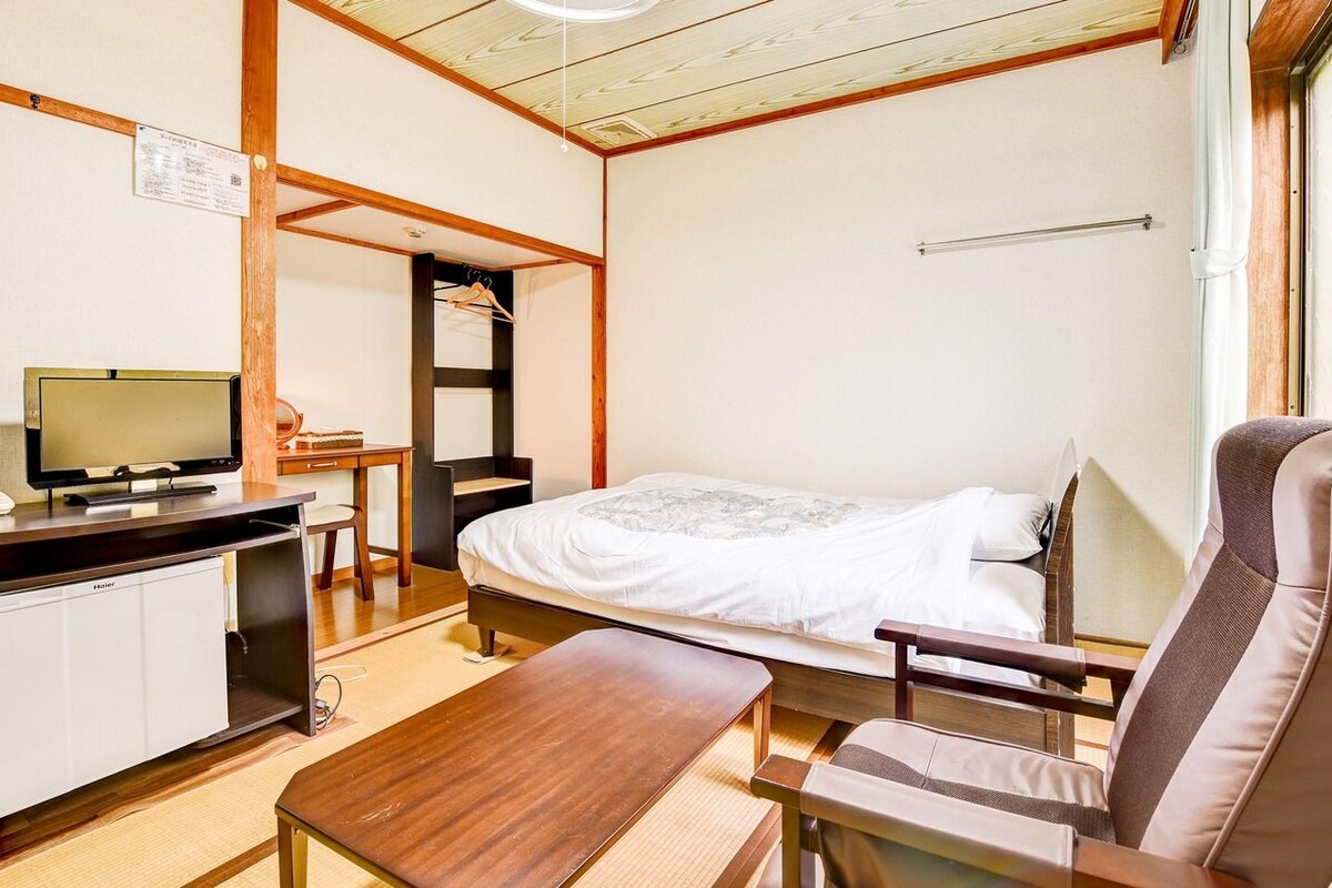 A small, cozy room with a bed, a desk, a chair, and a television.