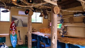 A rustic bar area with wooden furniture, a surfboard, and nautical decorations.
