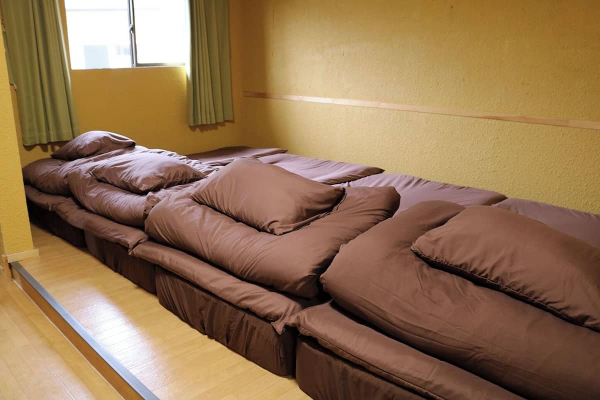 A single bed with brown bedding in a room with yellow walls and a window with green curtains.
