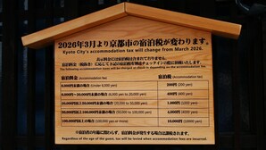 Ein Holzschild mit Informationen zu Steuern für Unterkünfte in Kyoto.