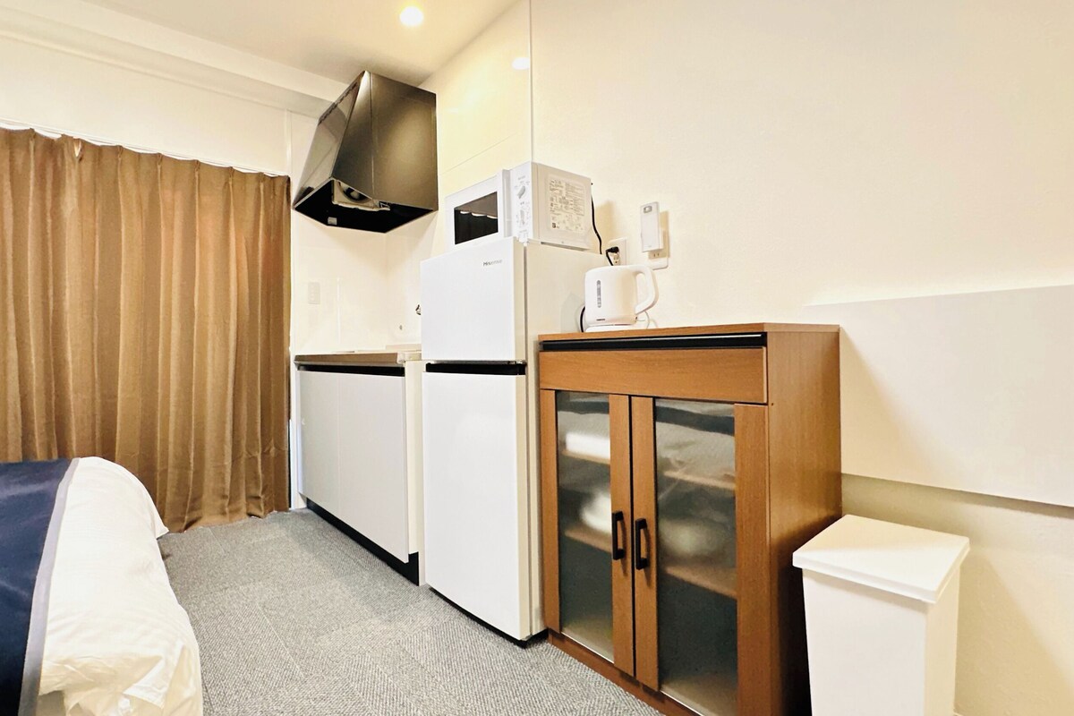 Habitación de hotel con una cama, una kitchenette con microondas, refrigerador y un mueble con puerta de vidrio.