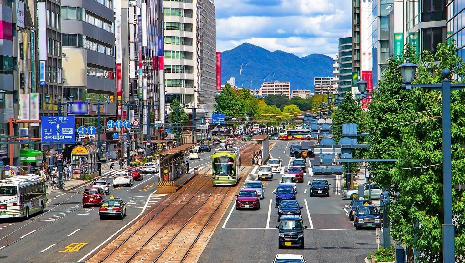 A busy urban street with tram tracks, vehicles, and buildings.