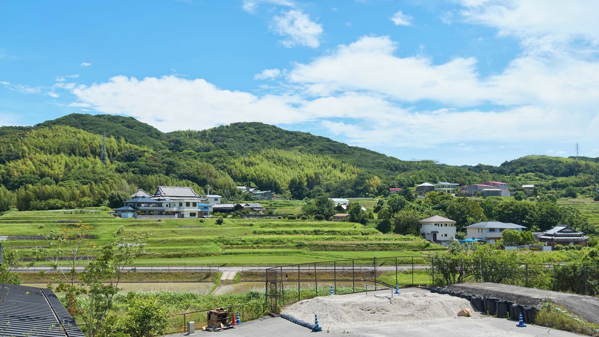 A rural landscape with houses, terraced fields, and a hill in the background.