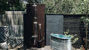 A modern outdoor shower enclosure with a built-in water heater, a metal tub, and a wooden fence.