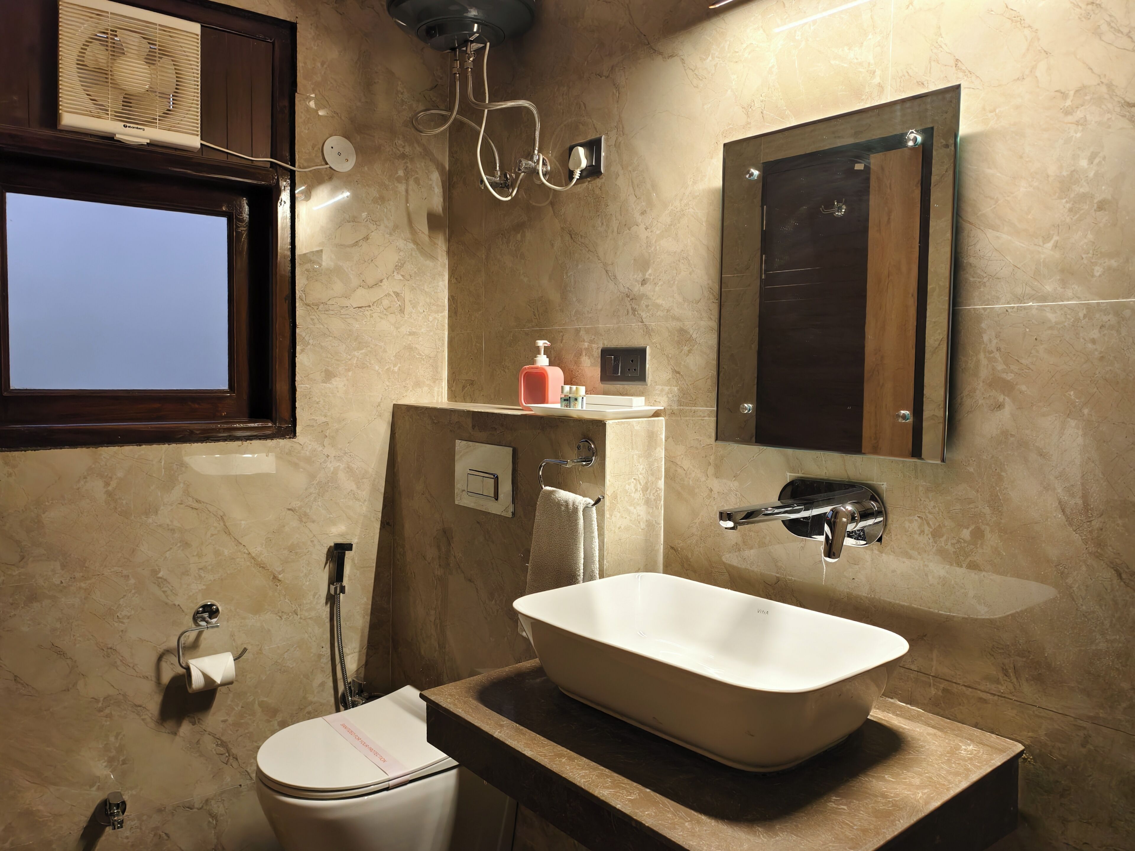 A bathroom with a toilet, a sink with a basin, a towel rack, a mirror, and a shower head.