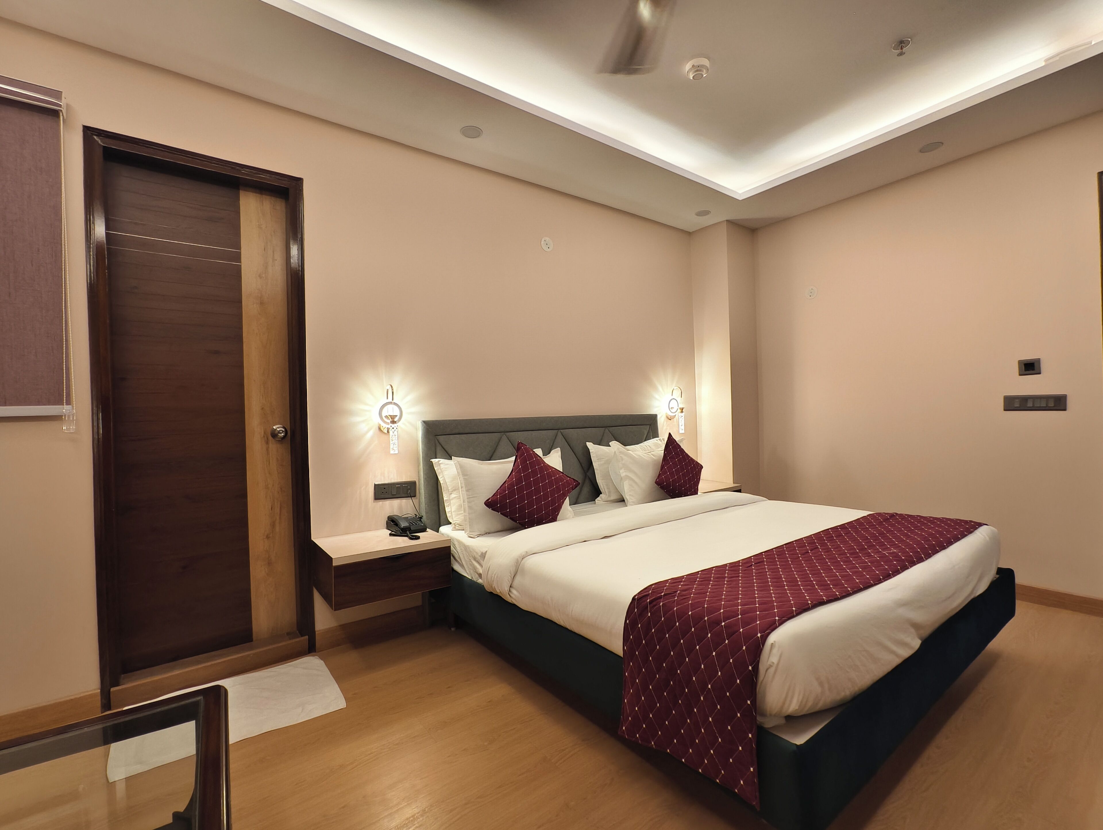 A hotel room with a bed, bedside tables, a nightstand, a wooden door, and a ceiling fan.