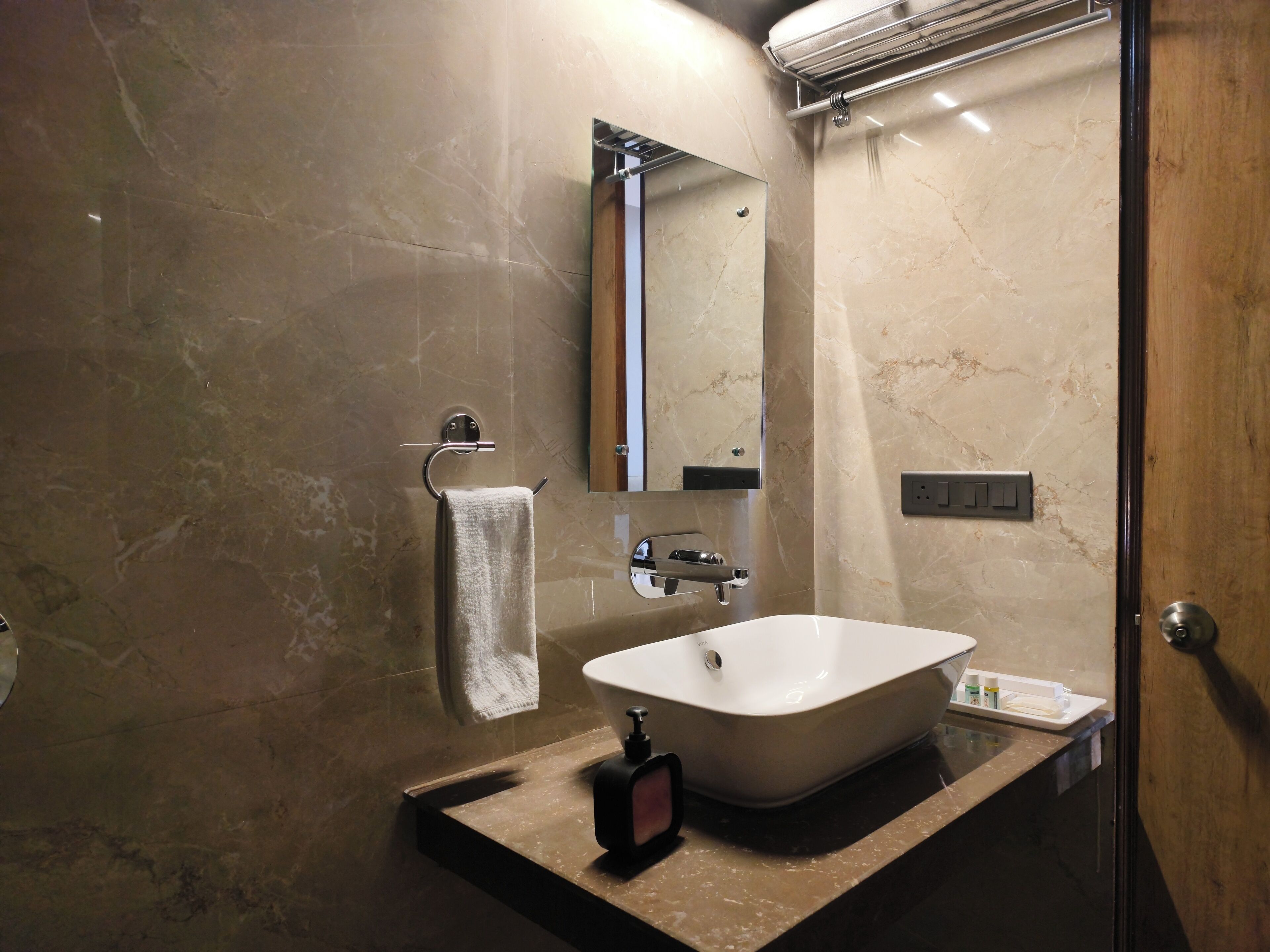 A bathroom with a marble wall, a sink, a mirror, and a towel rack.