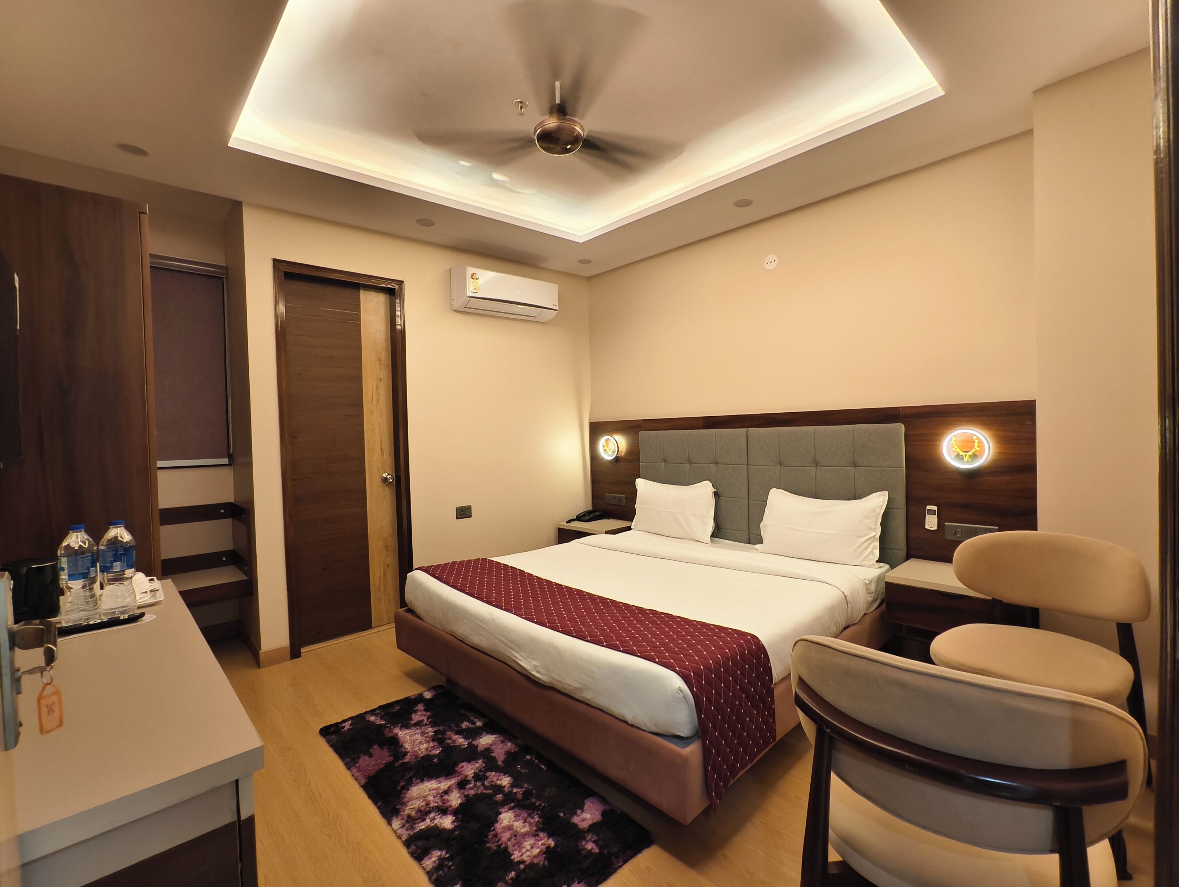Habitación de hotel con cama, escritorio, silla, unidad de aire acondicionado y ventilador de techo.