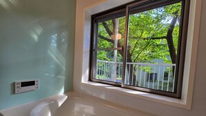 A bathroom with a bathtub, a window with a view of trees, and a thermostat on the wall. - AJ Villa (Atami)