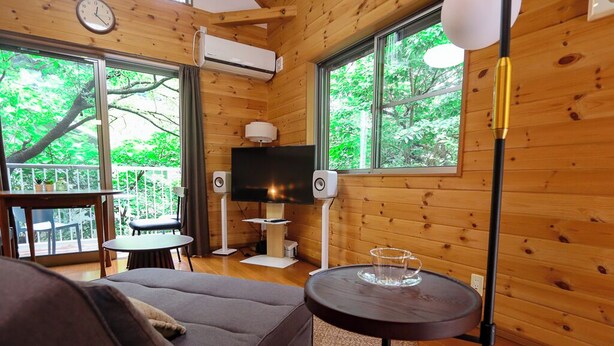 A wooden cabin interior with a sofa, a small round table, a TV, and large windows. - AJ Villa (Atami)