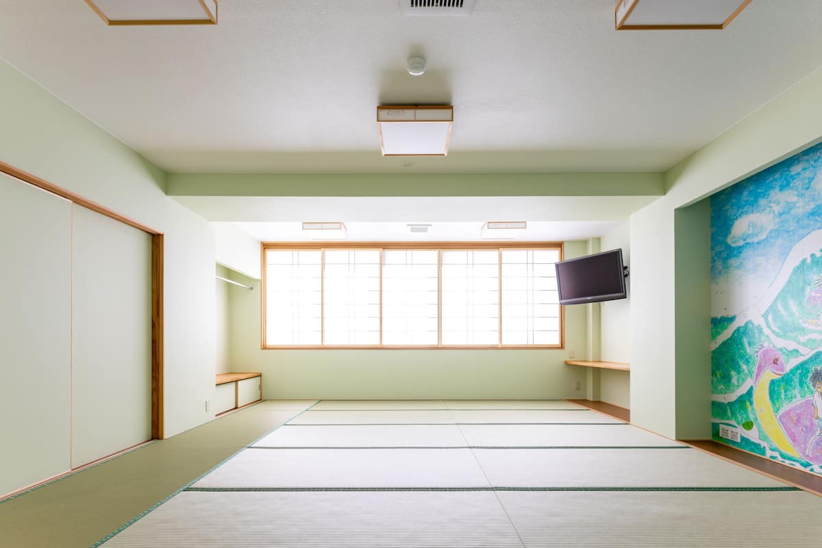 A tatami mat room with a television, tatami flooring, a sliding door, and a colorful mural.