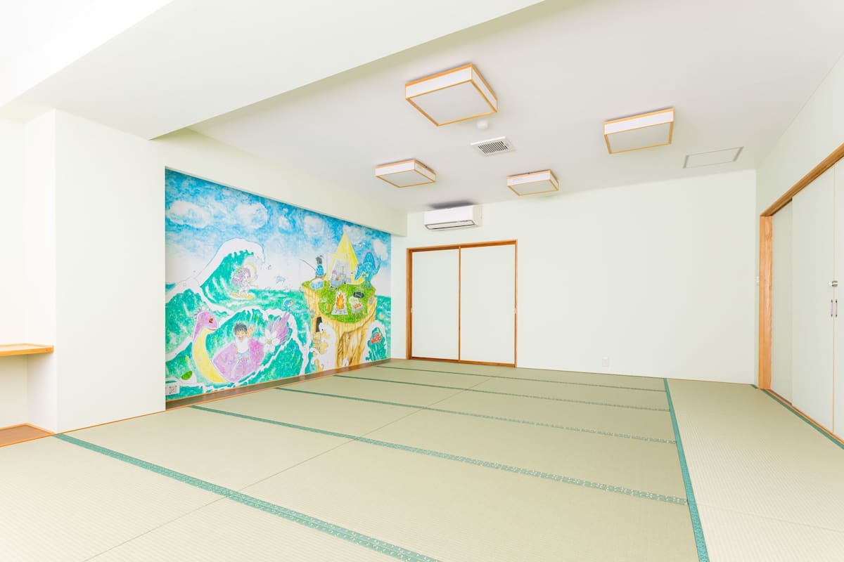 A room with tatami flooring, a large colorful mural, a sliding door, and recessed lighting.