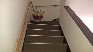 A staircase with carpeted steps, a wooden handrail, and a wall-mounted light fixture. - Ryokan Urashima (Echizen)