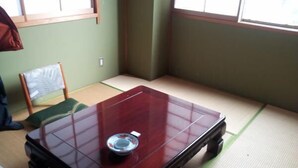 A tatami mat room with a low wooden table and a green cushion. - Ryokan Urashima (Echizen)