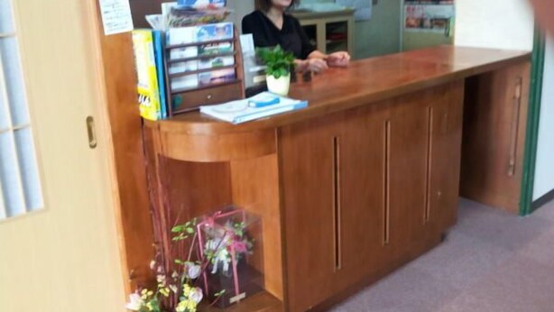 A reception desk with a wooden finish, a potted plant, and a bulletin board with papers. - Ryokan Urashima (Echizen)
