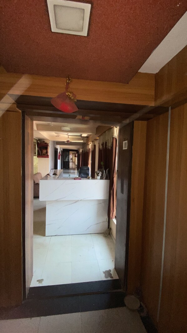 A hotel lobby with a reception desk, a red ceiling light, and a tiled floor. - Hotel Anand Palace Inn (Ahmedabad)