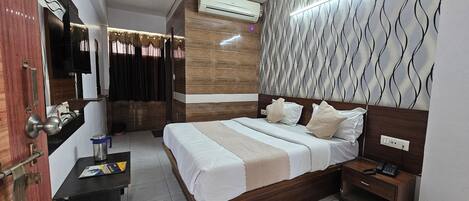 A hotel room with a bed, bedside table, nightstand, and an air conditioning unit.