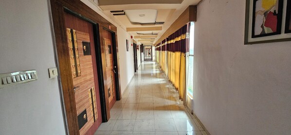 A long, narrow hallway with wooden doors on one side and a window with curtains on the other.