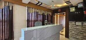 A hotel reception area with a marble counter, curtains, a ceiling fan, and a wooden ceiling.
