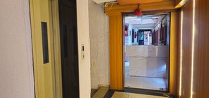 A hotel hallway with a marble floor, a wooden door, and a ceiling light fixture. - Hotel Anand Palace Inn (Ahmedabad)