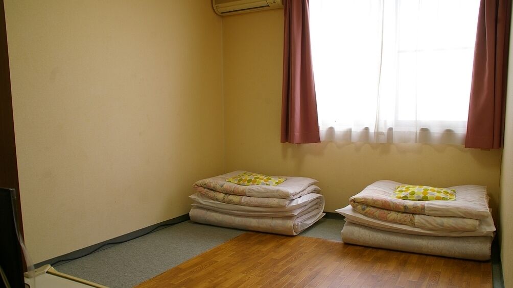 A room with two beds, a window with curtains, and a radiator.