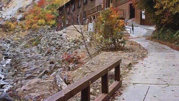 A wooden building with a stone pathway leading to a wooden bridge over a rocky stream. - Masugataya (Yonezawa)
