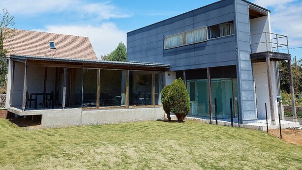Ein modernes, zweistöckiges Haus mit großen Fenstern, einer überdachten Terrasse und einem gepflegten Rasen.