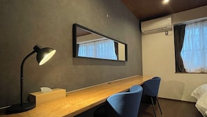 Una habitación moderna con escritorio, dos sillas, espejo, lámpara, equipo de aire acondicionado y ventana con cortinas.