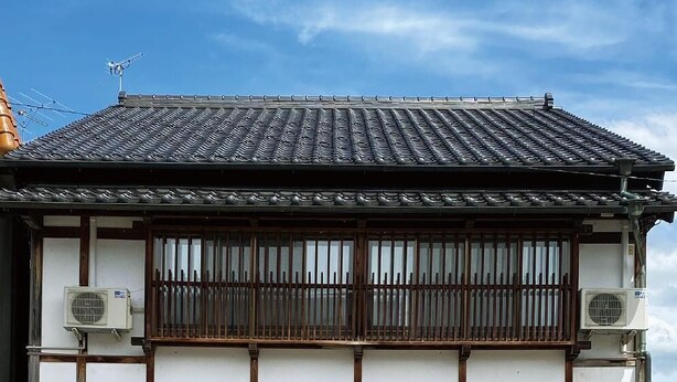 Un edificio japonés tradicional con techo de tejas, balcón de madera y ventanas grandes.