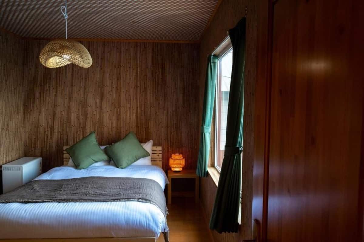 Ein Zimmer aus Holz mit einem Bett, einem Nachttisch mit Lampe und einem Fenster mit Vorhängen.