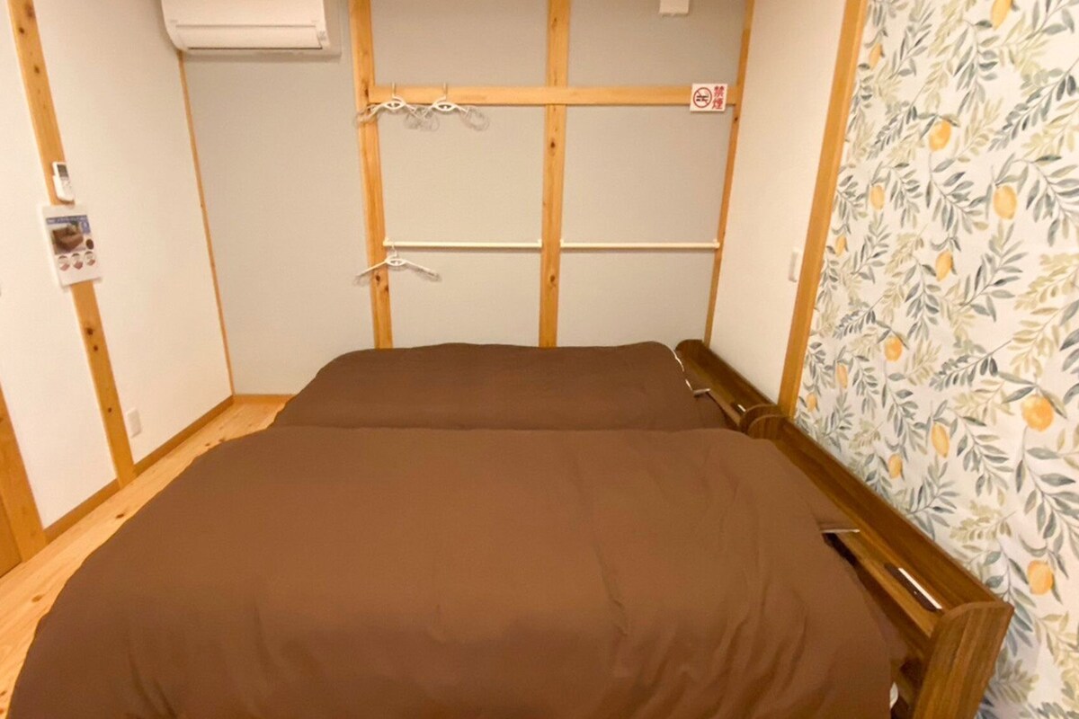 Een kleine eenpersoonskamer met een houten hoofdeinde, een wandairconditioner en een bordje ‘niet roken’.