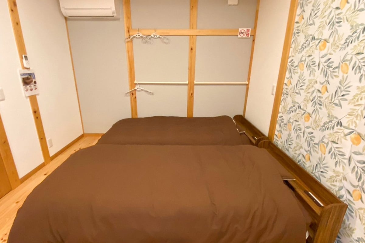 A small, single-bed room with a wooden headboard, a wall-mounted air conditioner, and a no-smoking sign.