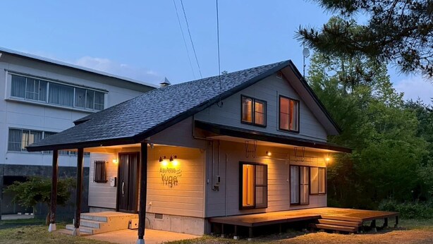 Una casa de dos pisos con un porche cubierto, una banca y un letrero que dice 'Asy base Yuge'.