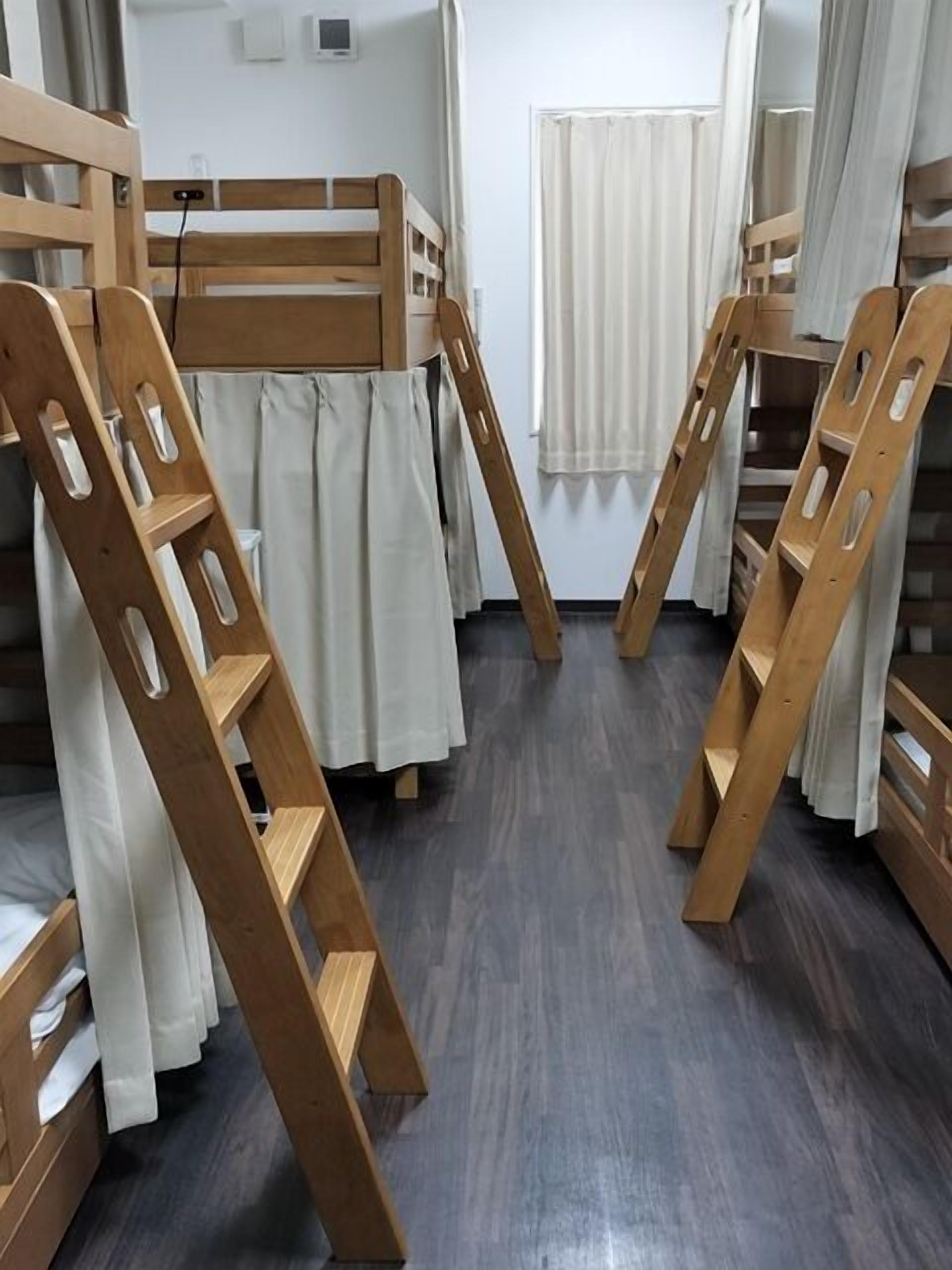 Dormitorio con literas, escaleras de madera, una cortina blanca y una ventana con cortinas blancas.