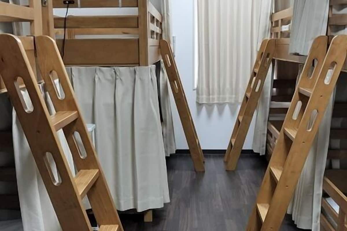 Quarto com beliche, escadas de madeira, uma cortina branca e janela com cortinas brancas.