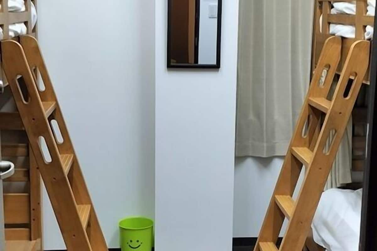 Quarto com duas beliches, uma lixeira verde, um espelho e uma janela com cortinas.