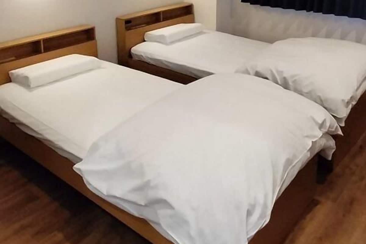 Quarto com duas camas de madeira, roupa de cama branca e luminárias fixadas na parede.