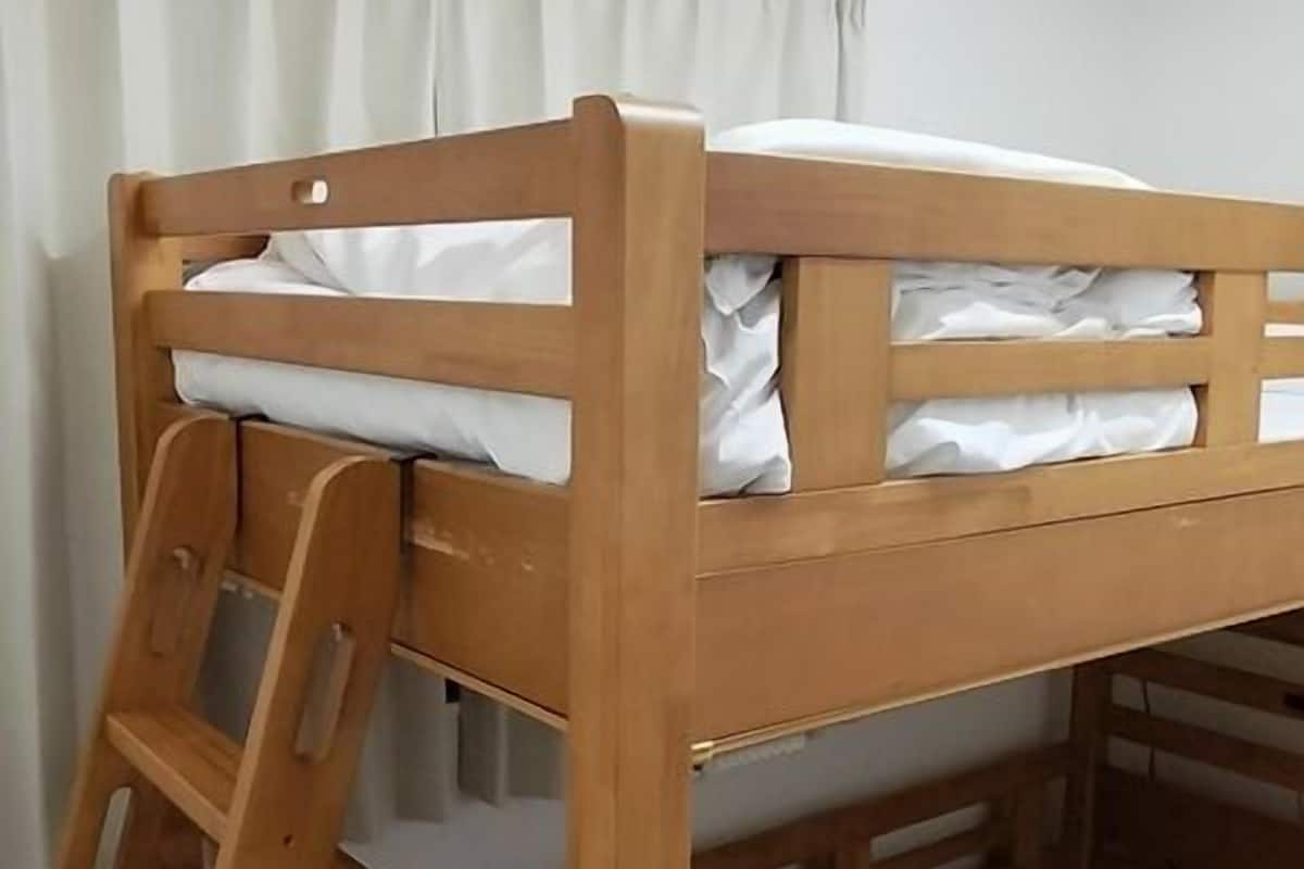 Uma cama beliche com escada de madeira, um colchão e piso de madeira.