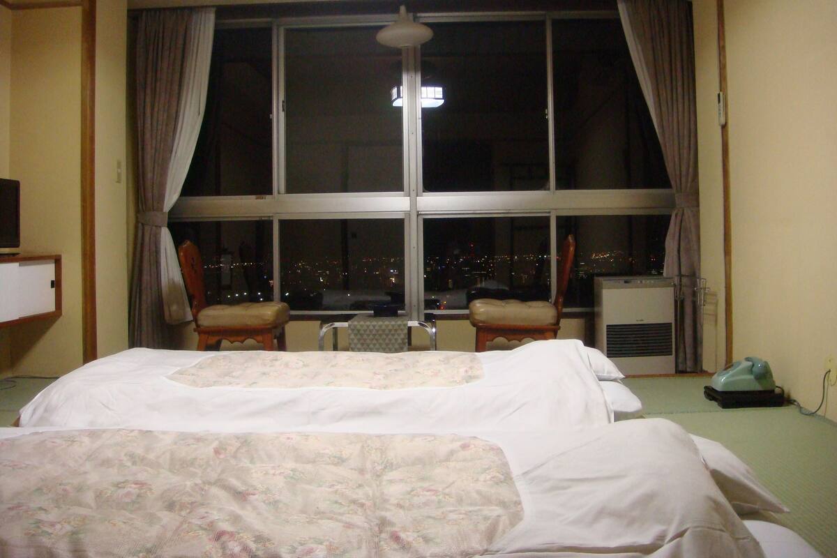 Una habitación de hotel con un ventanal grande, una cama, dos sillas y un calentador.