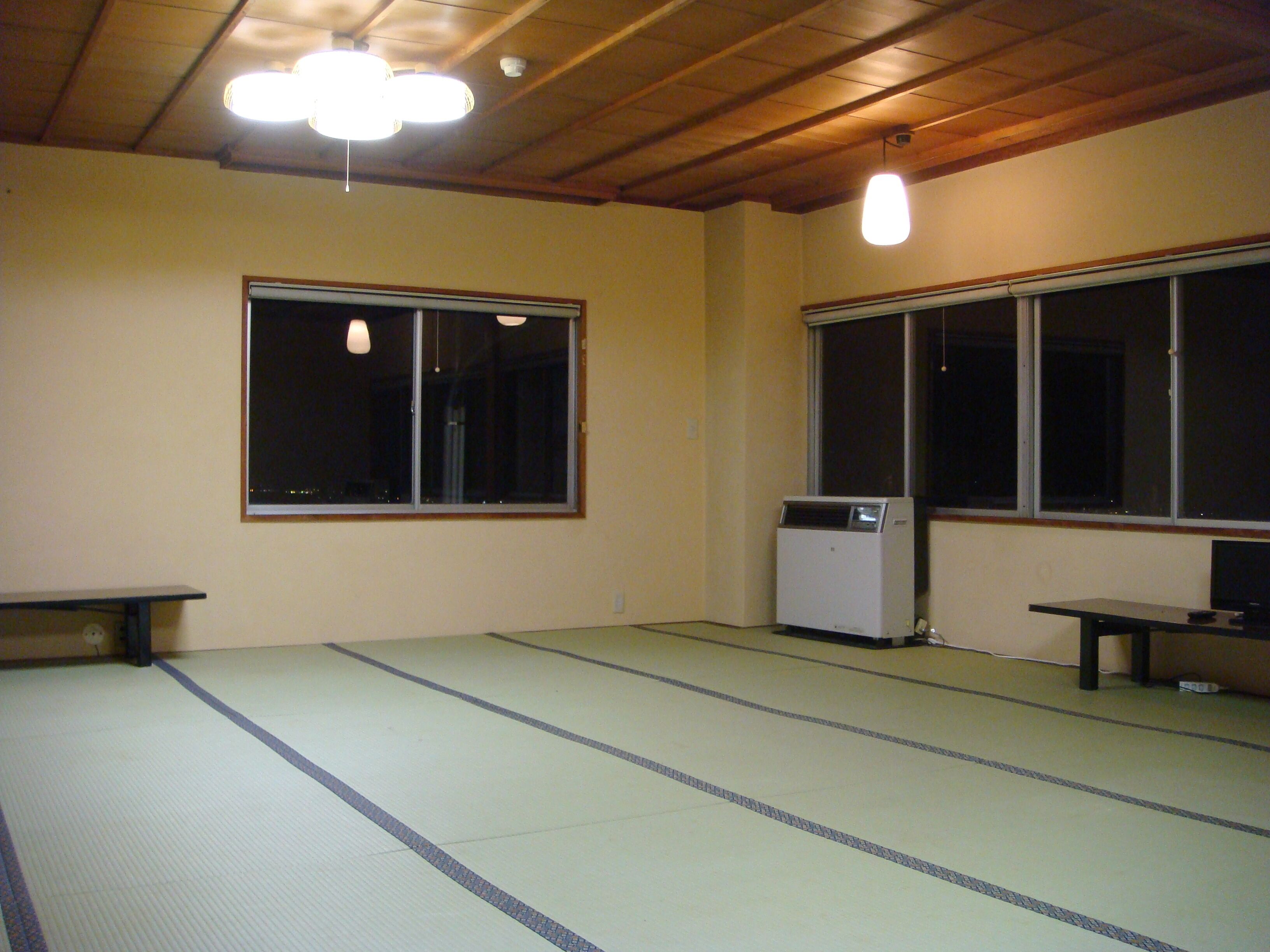 A room with tatami flooring, a heater, a bench, and two windows.