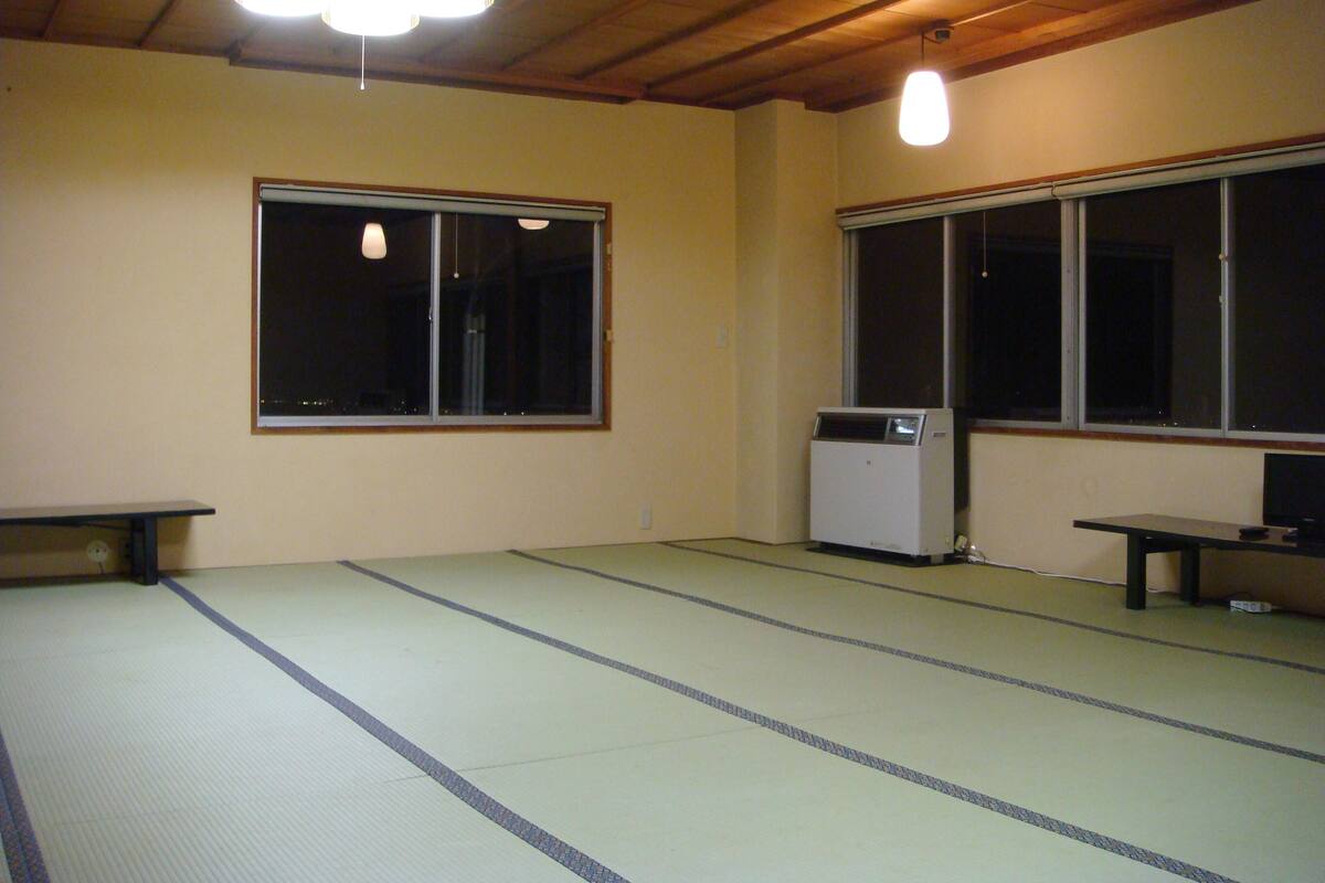 Una habitación con suelo de tatami, un calentador, un banco y dos ventanas.
