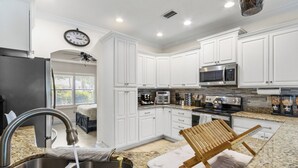Una cocina con armarios blancos, un refrigerador de acero inoxidable, un microondas y una estufa.