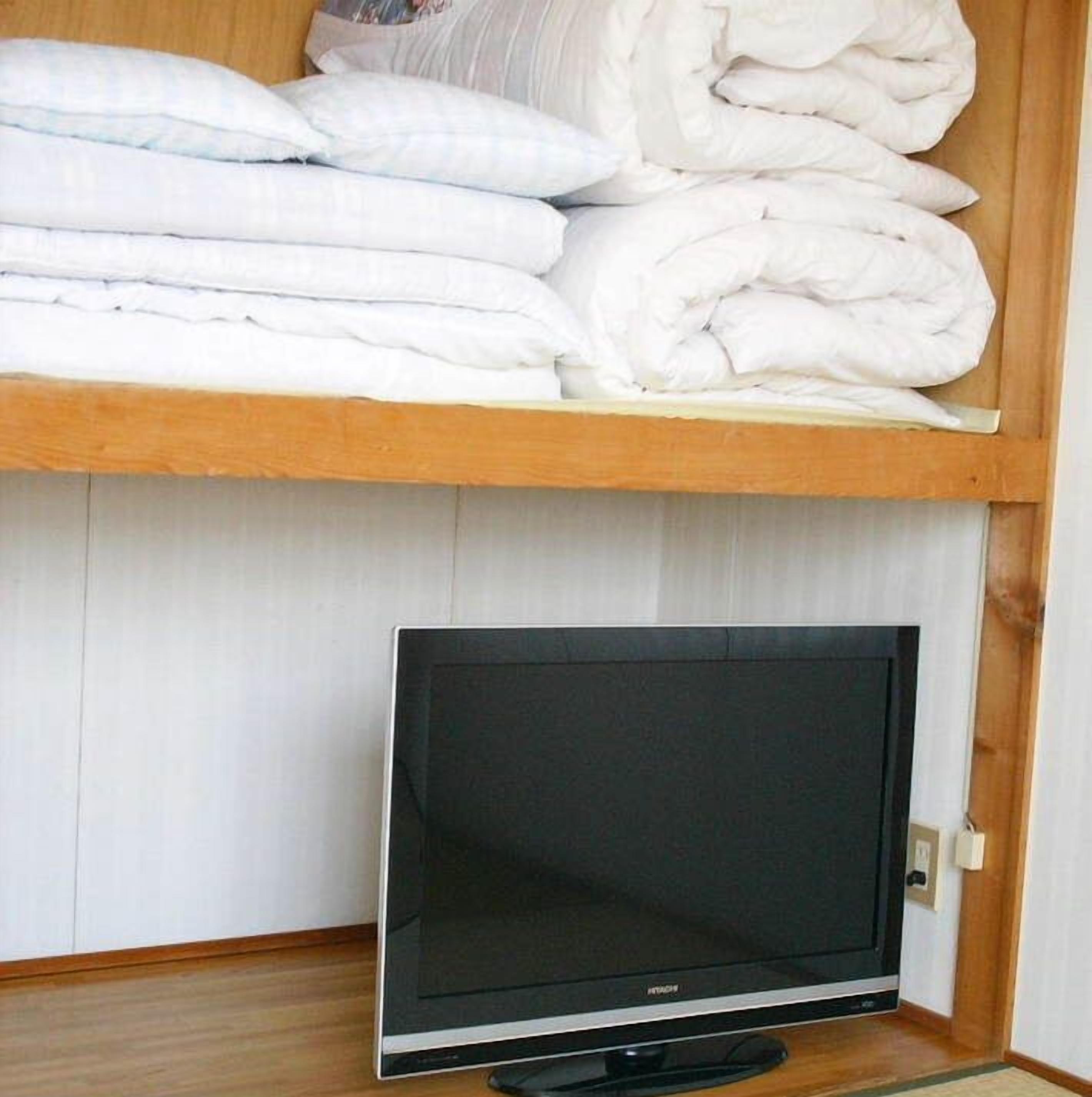 Ein Zimmer mit Fernseher auf einem Schrank, einem Holzboden mit gefalteten Decken und einer weißen Wand.