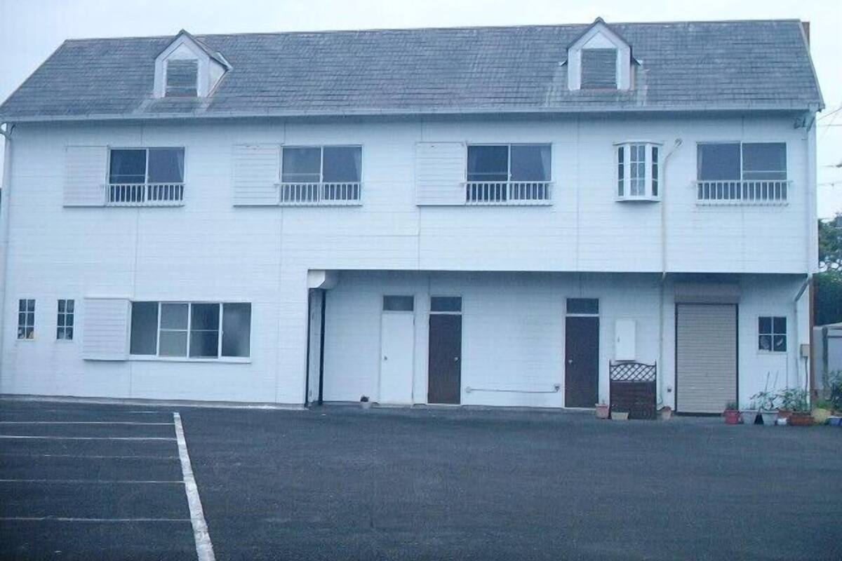 Un edificio de dos pisos con garaje, un porche pequeño y un estacionamiento.