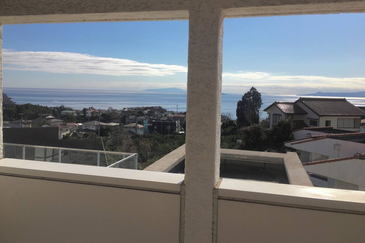 Vista da janela para uma cidade costeira com casas e céu claro.