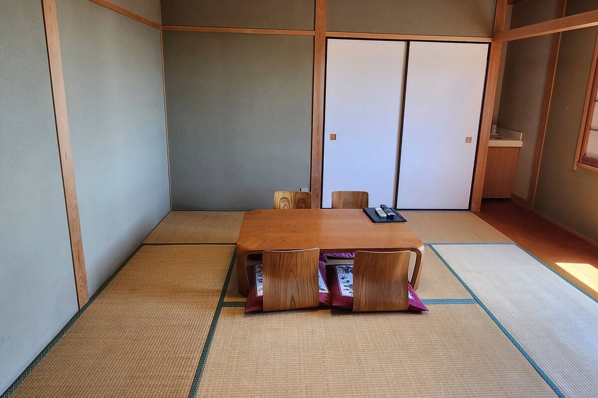 Um espaço com tatames, mesa de madeira e cadeiras, portas deslizantes e uma janela.