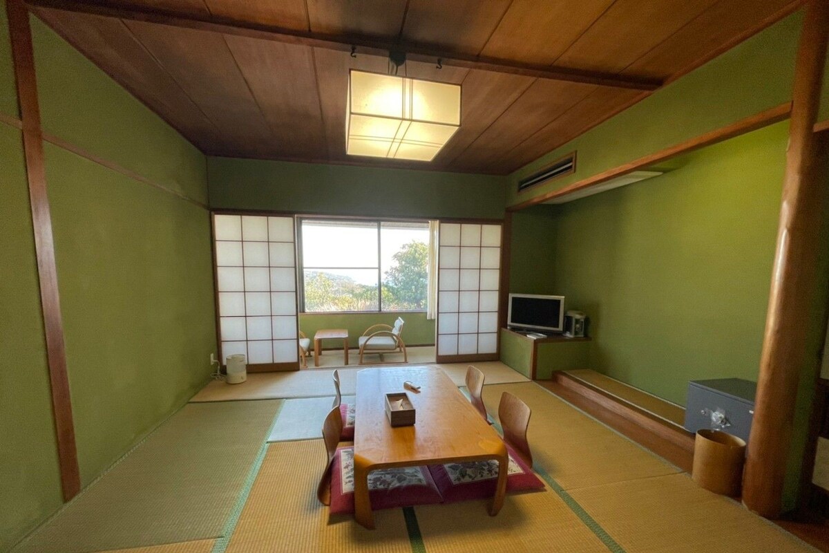 A tatami mat room with a low table, chairs, a TV, and sliding doors.