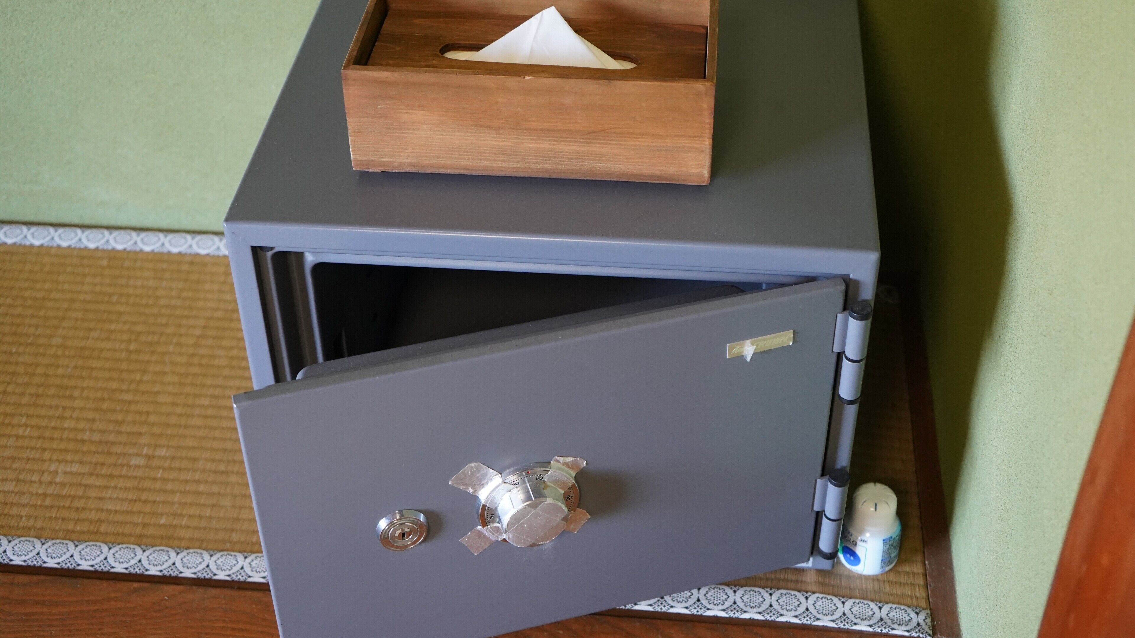 A grey safe with a wooden box on top, a keyhole, and a small lock on the side.