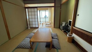 A traditional Japanese room with tatami flooring, a low table, a sliding door, and a view of the outside.
